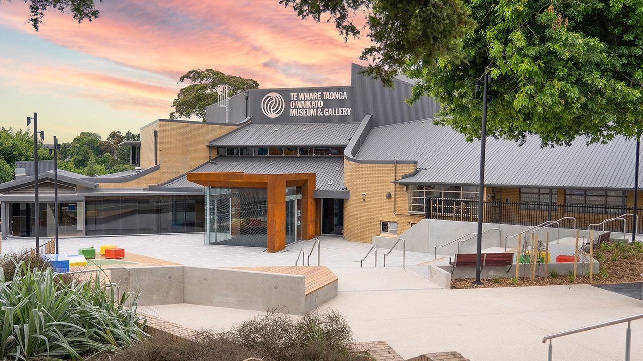 Te Whare Taonga o Waikato Museum and Gallery building at dusk, framed by a soft pale pink sunset sky.